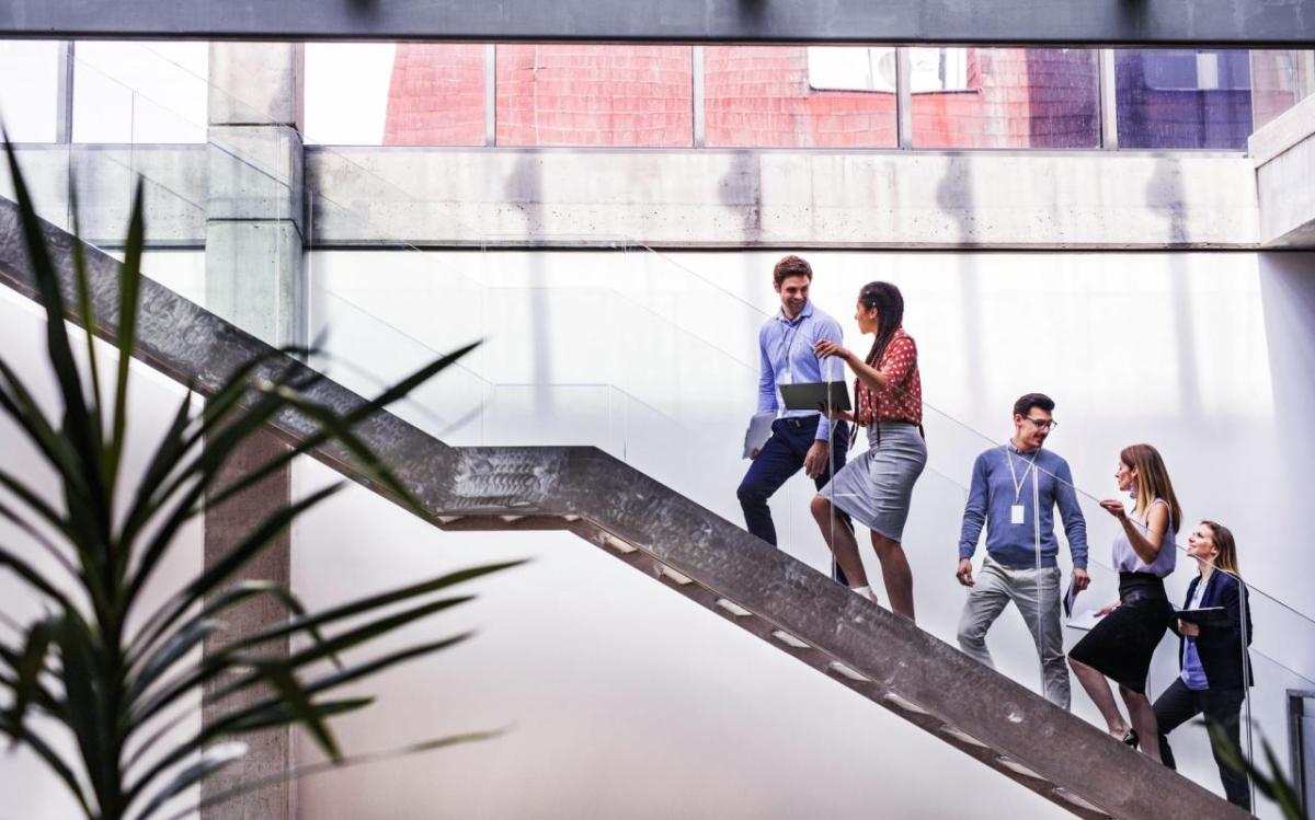 People talking while climbing a staircase with clear railing sides.