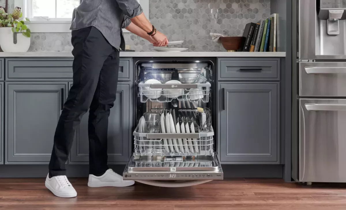 A person unloading clean dishes from a LG brand dishwasher in a kitchen.