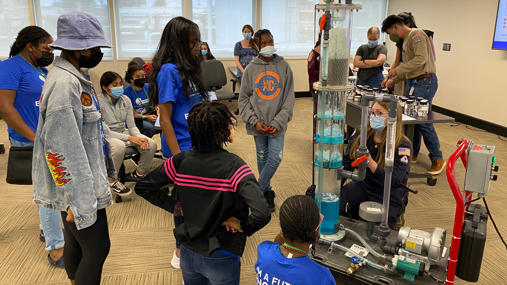 a volunteer shows a group of children how the distillation tower model works