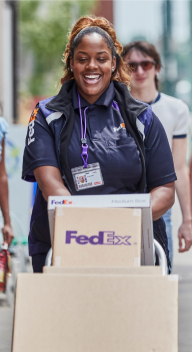 A person in FedEx uniform wheeling a stack of boxes on a dolly.