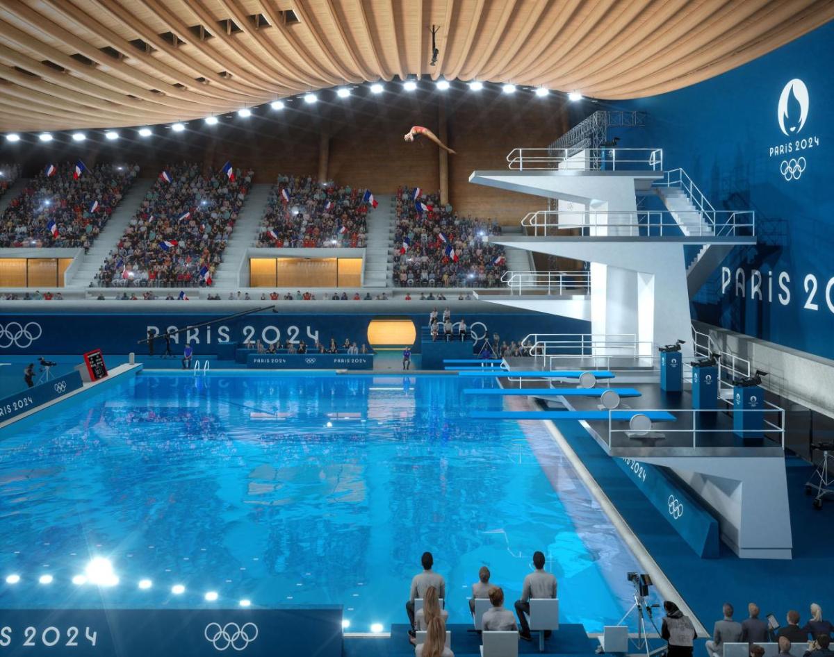 A person diving from a high platform in an aquatics center. People in the stands watching.