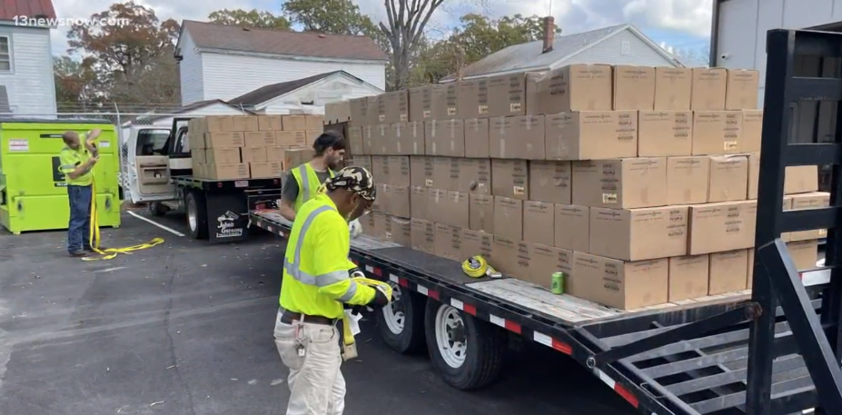 Trailers with stacked boxes in a parking lot, people in high-vis clothing around the trailers. 