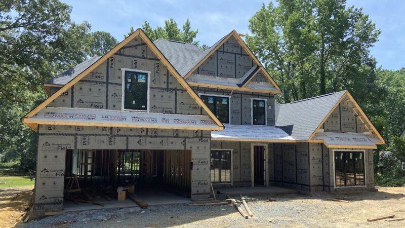 A two-story home being built. Dense trees behind it.