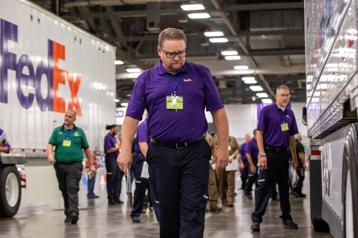 driver in purple shirt and glasses inspects a truck