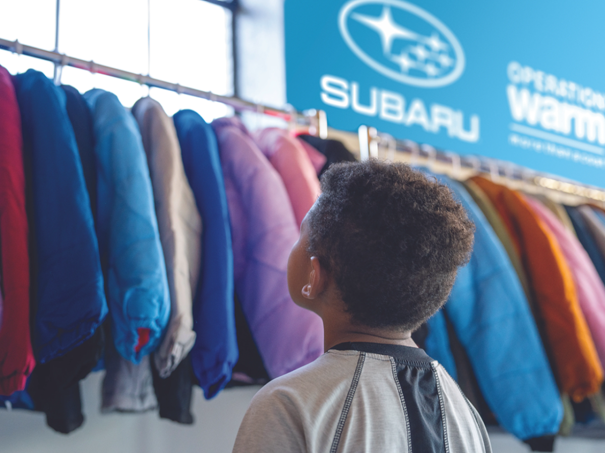 child looks up at hanging coats