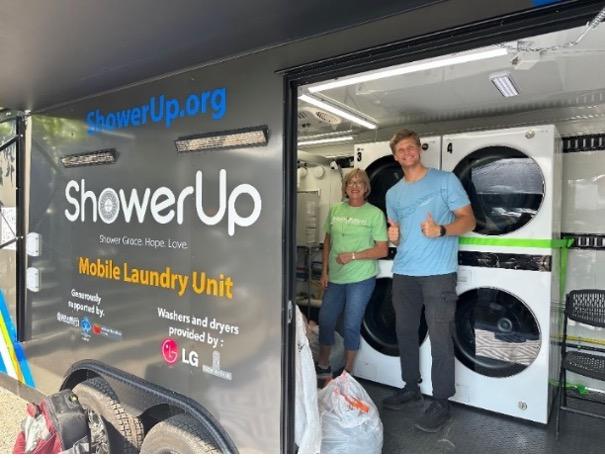 Two people smiling inside an open ShowerUp mobile laundry unit