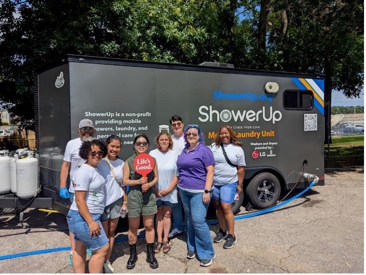 A small group of people posed together outside a ShowerUp mobile laundry unit