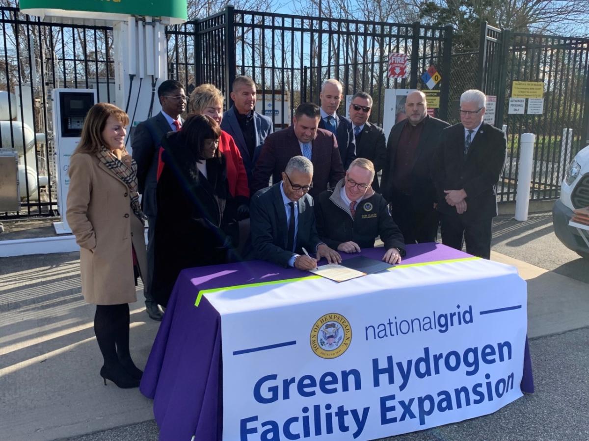 People posing for picture around table with banner reading: Green Hydrogen Facility Expansion