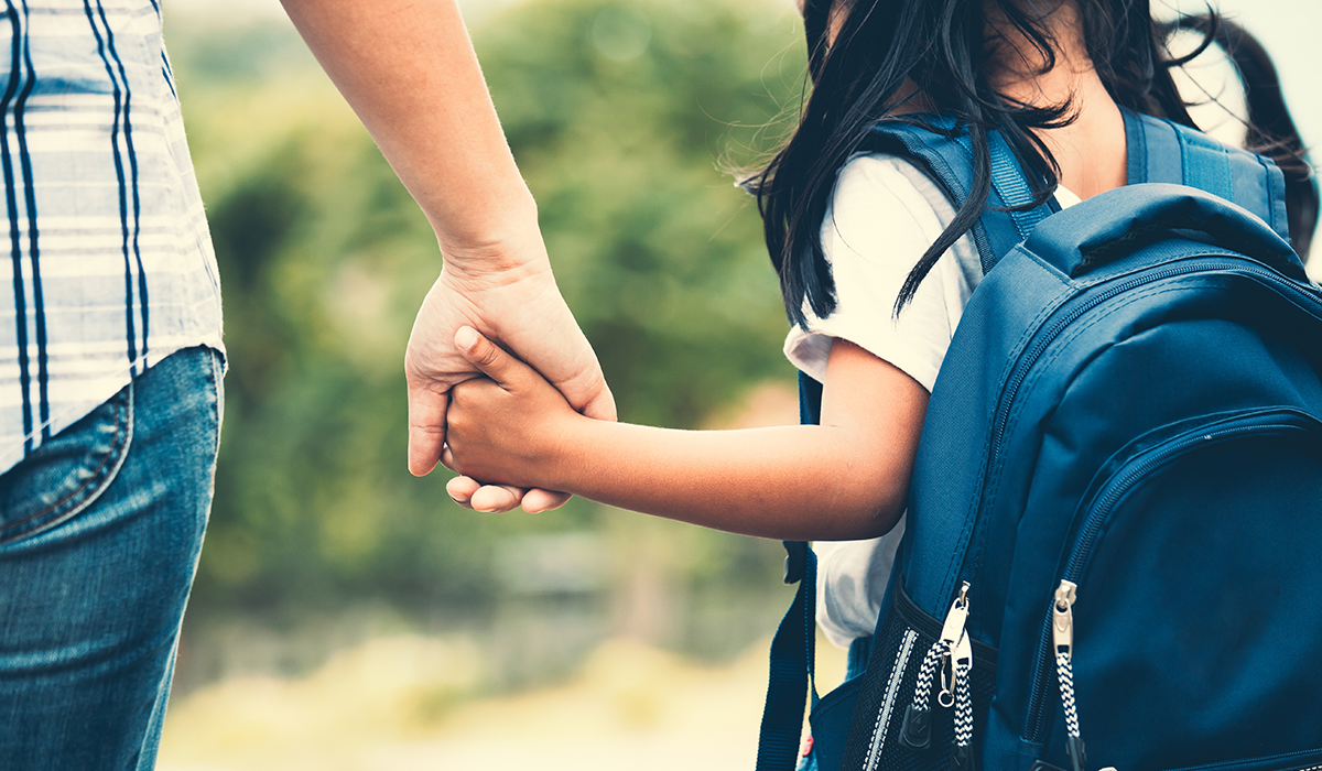 child wearing a backpack holding a grown-up's hand