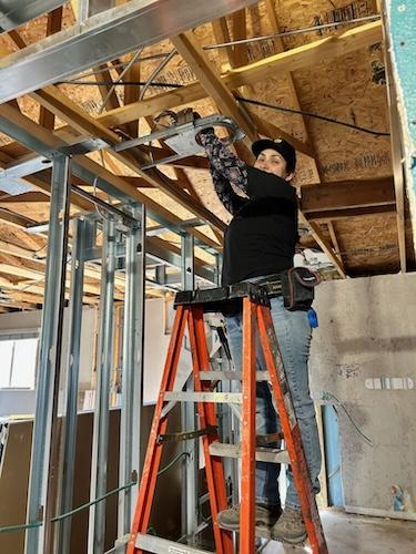 Maria on a ladder doing electrical work.