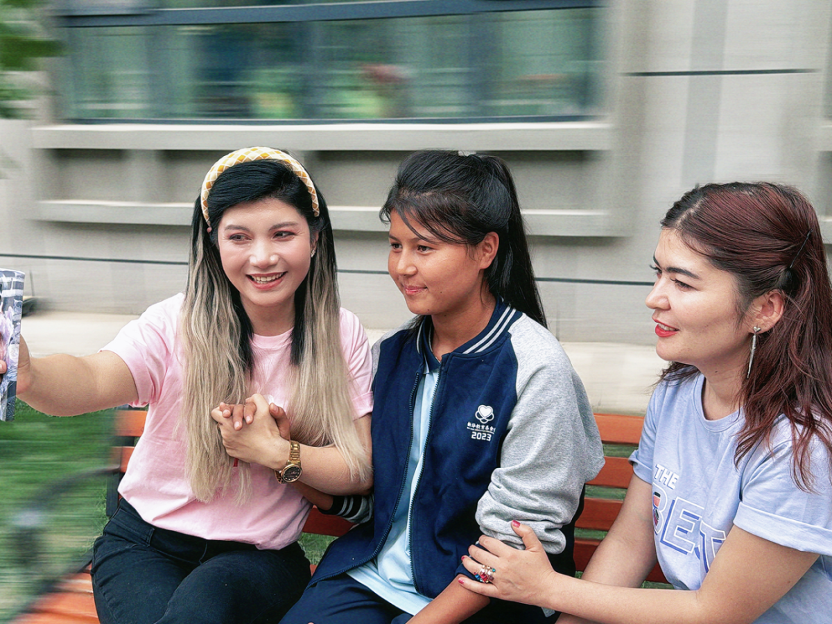 Three students sitting on a bench together and smiling
