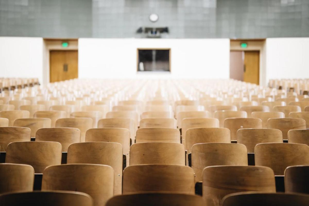 An empty auditorium with rows of wood back seats.