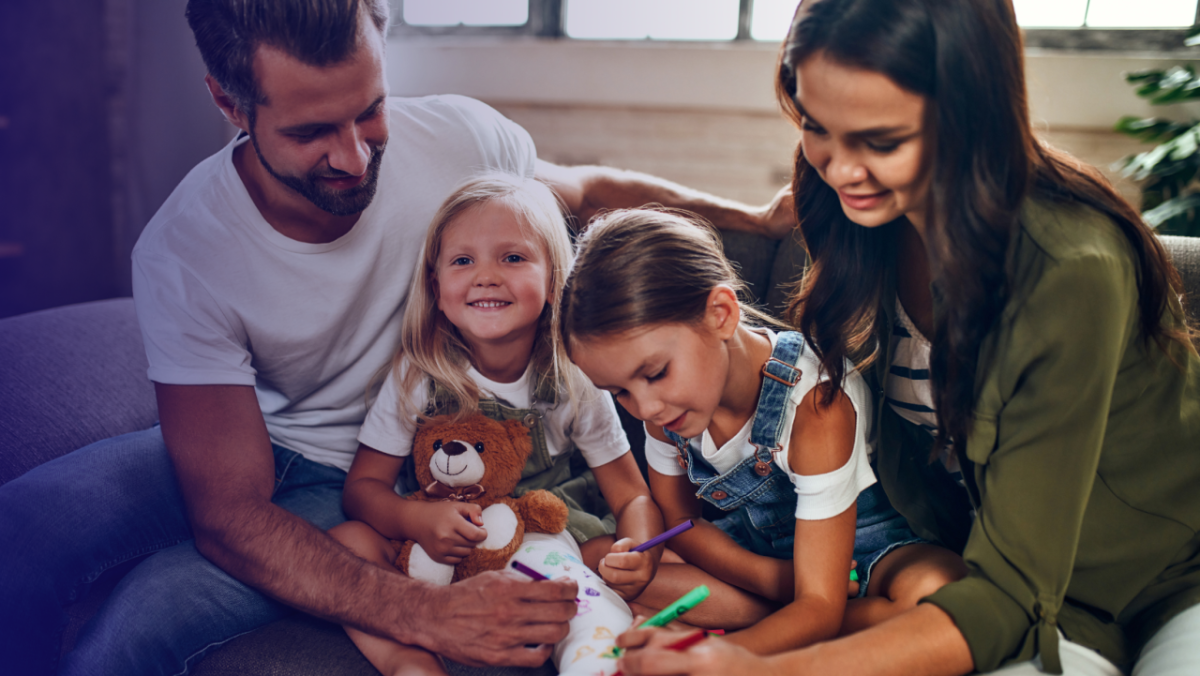 Two adults sitting on a couch with two children writing on stuffed bears