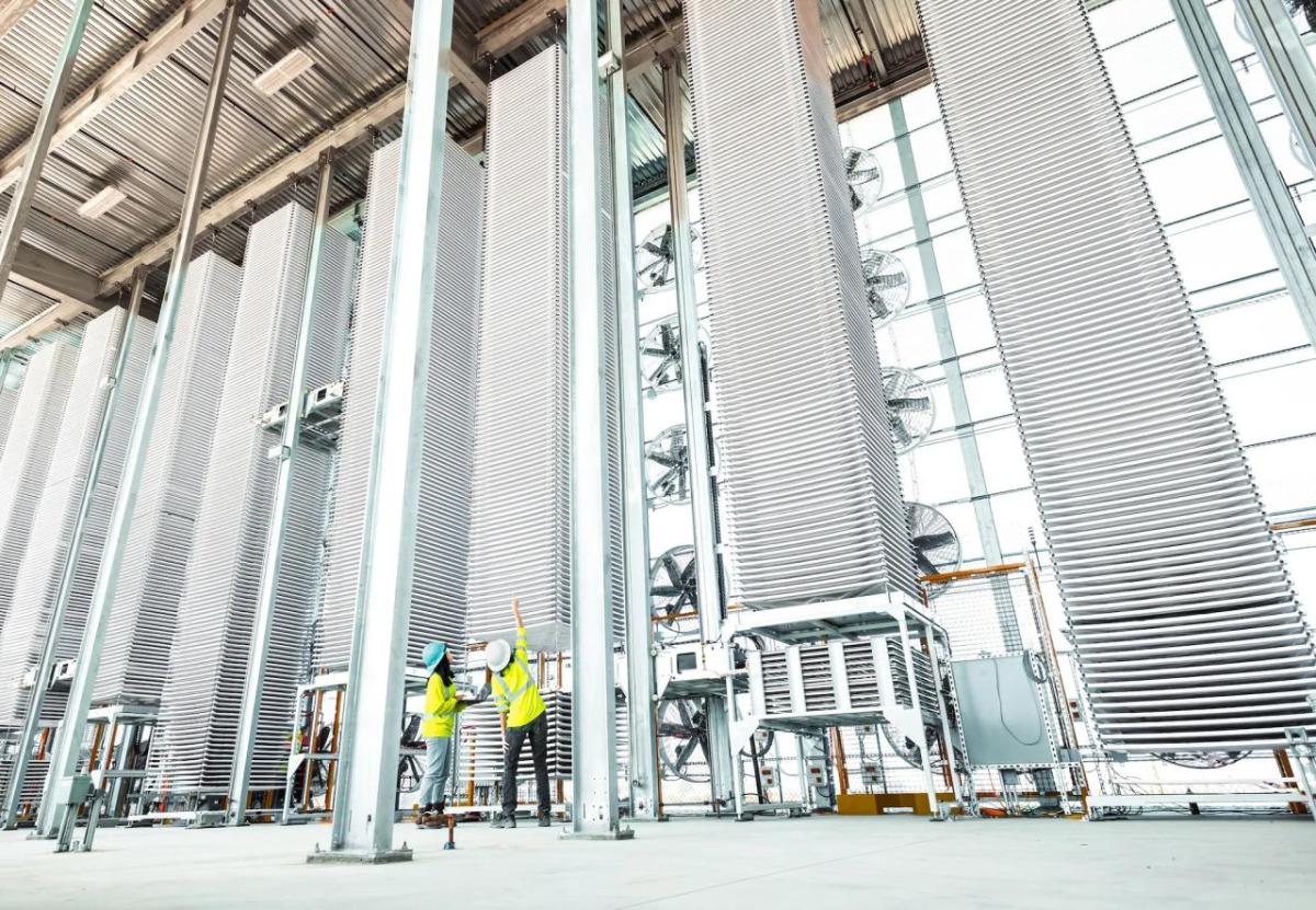 Photo by Heirloom Two people in high-vis vests looking at a tall stack of metal sheets in a row of other stacks.
