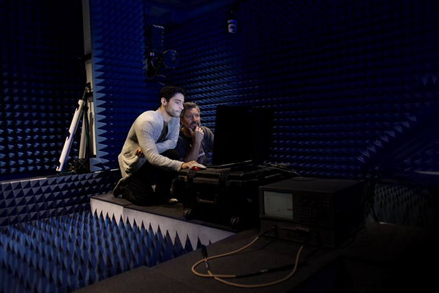 Two people surrounded by soundproof foam looking at the same computer screen.