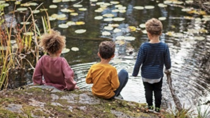 Three children playing on the bank of a waterway.