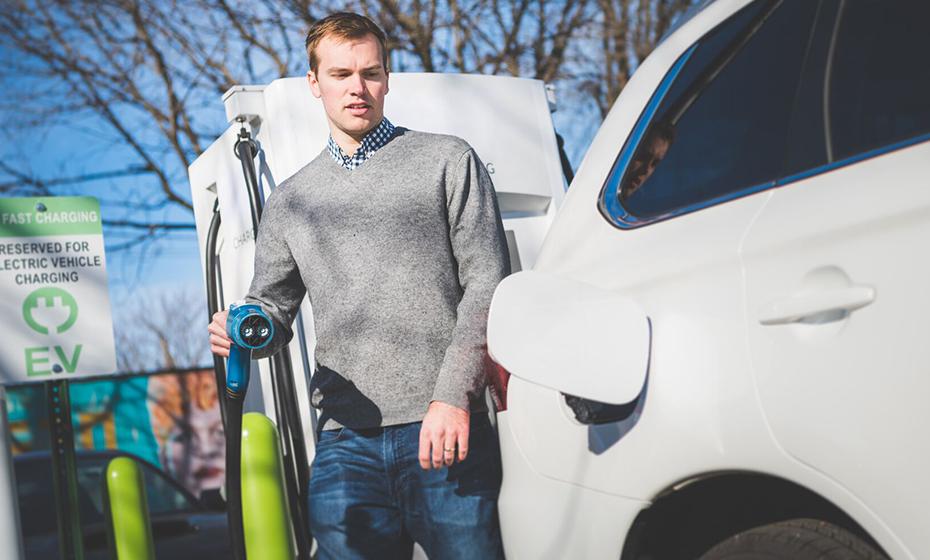 A person with a plug in one hand next to an open cover on an electric vehicle.