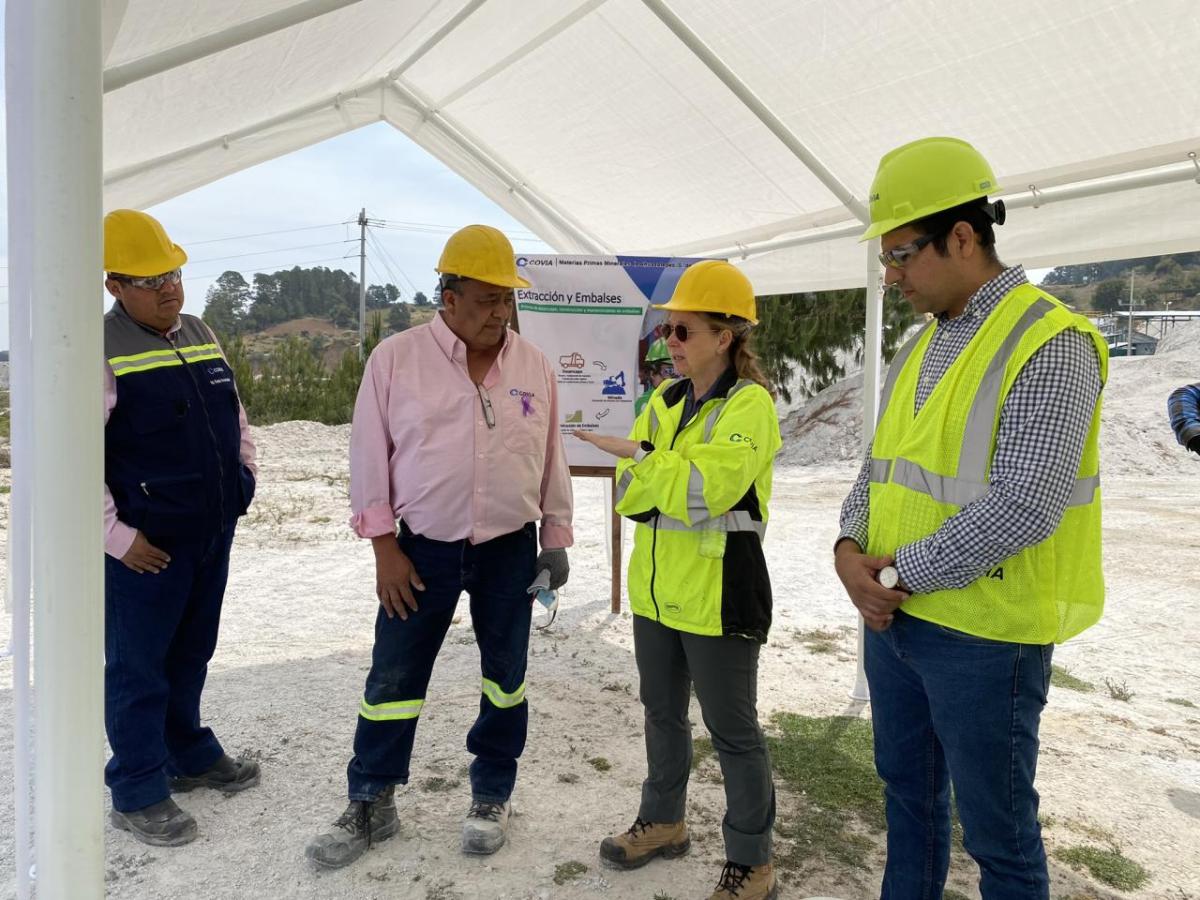 Four people in high-vis vests and hard hats talking under a canopy