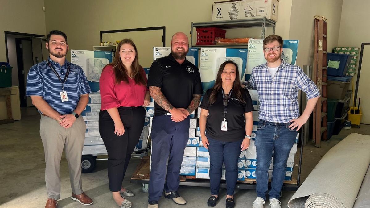 A group of five posed in front of stacks of boxed fans.