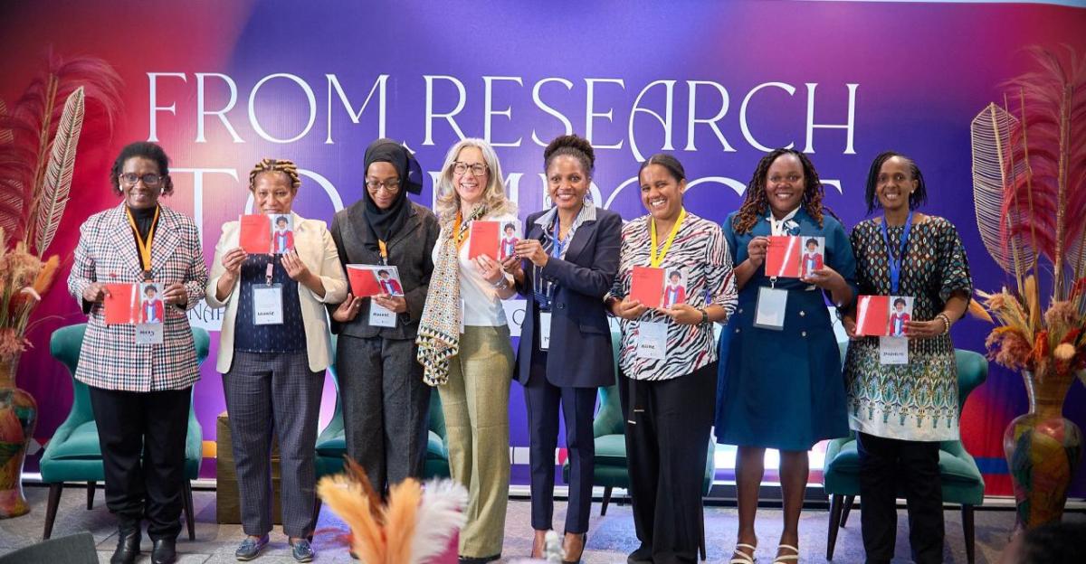 Eight people on a stage, each holding up the same photo