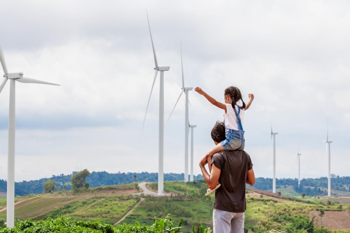 child on adults shoulders looking at wind turbines
