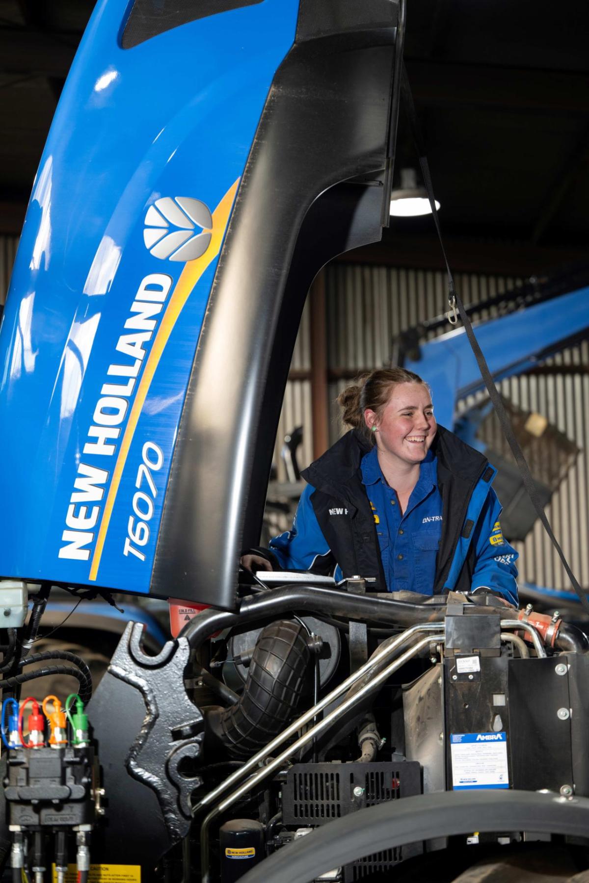 A smiling person looking under the hood of a farming tractor.
