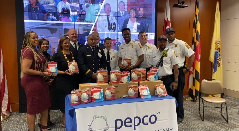 A group of people, some in fire/EMS uniform, behind a table of smoke detectors and a pepco banner.