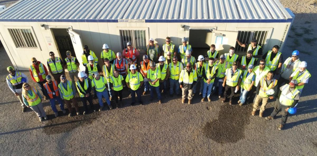 a large team of people, all wearing safety gear, outside a mobile trailer.