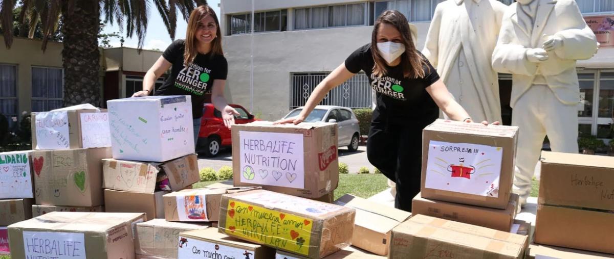 Two volunteers stand outside behind many stacked and hand decorated boxes