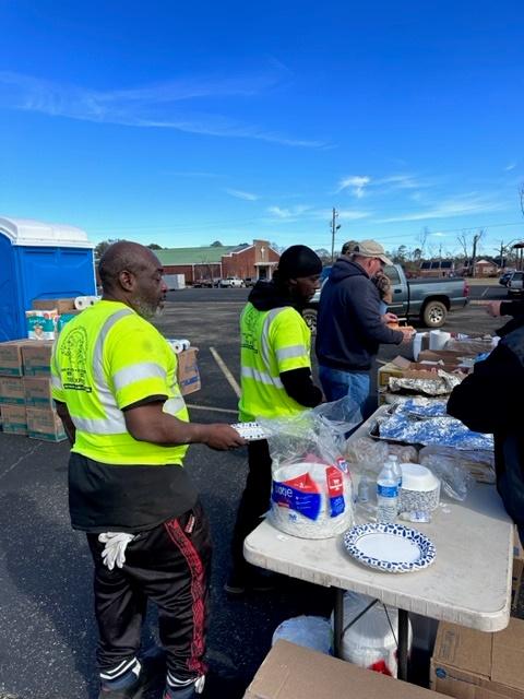 People in line being served food in a parking lot.