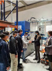 A group of people in protective masks in an industrial setting. Two hold hands.