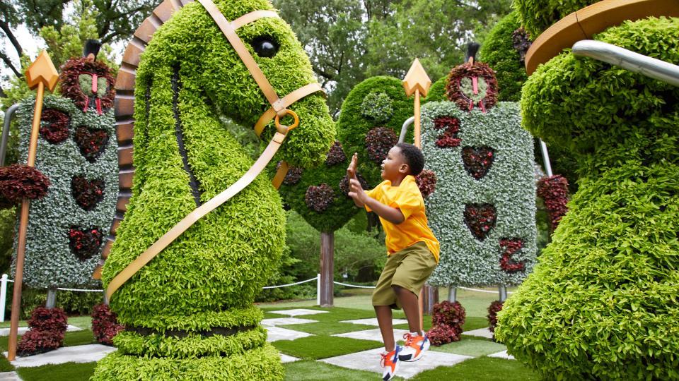 A child playing in a garden with chess piece shaped hedges.