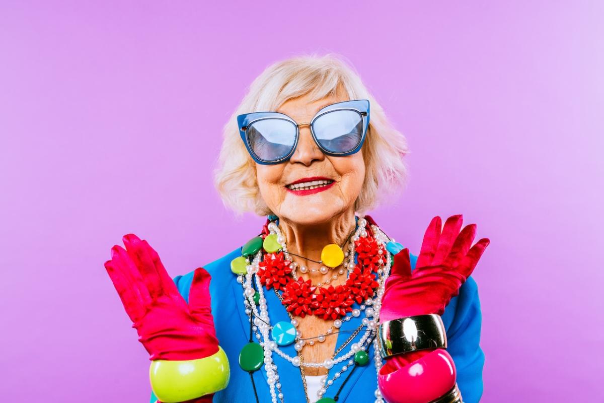Older, smiling woman wearing big sunglasses and rainbow pride colors for accessories.