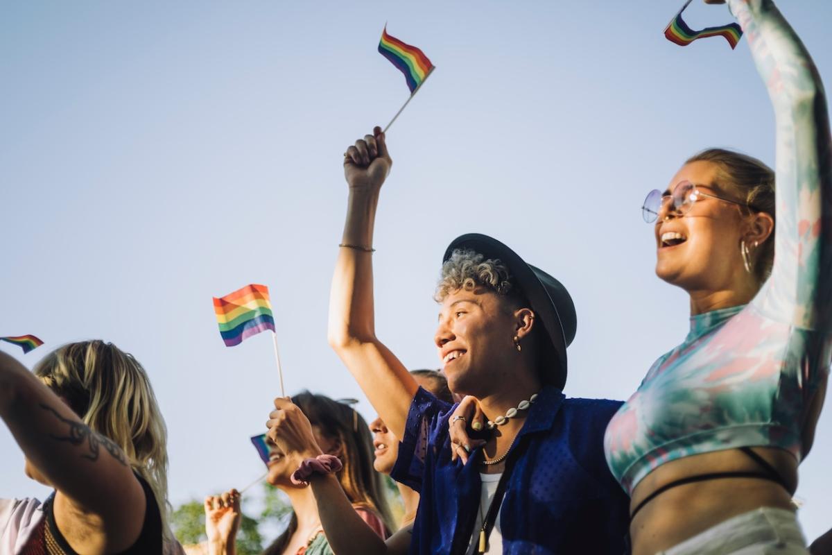 A group of individuals that are smiling and holding small rainbow flags.