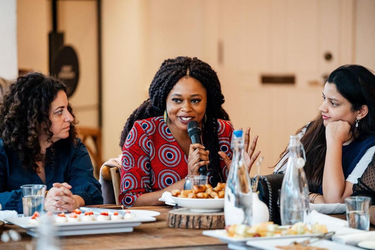 People seated at a dining table. One speaking with a microphone.