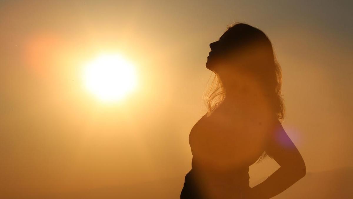 woman leans back in silhouette against a strong orange sun
