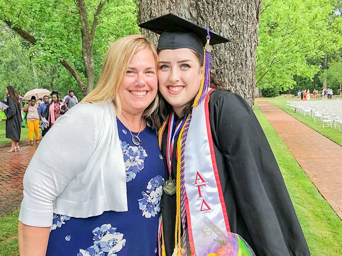 Danielle in a graduation cap and gown outside, hugging another