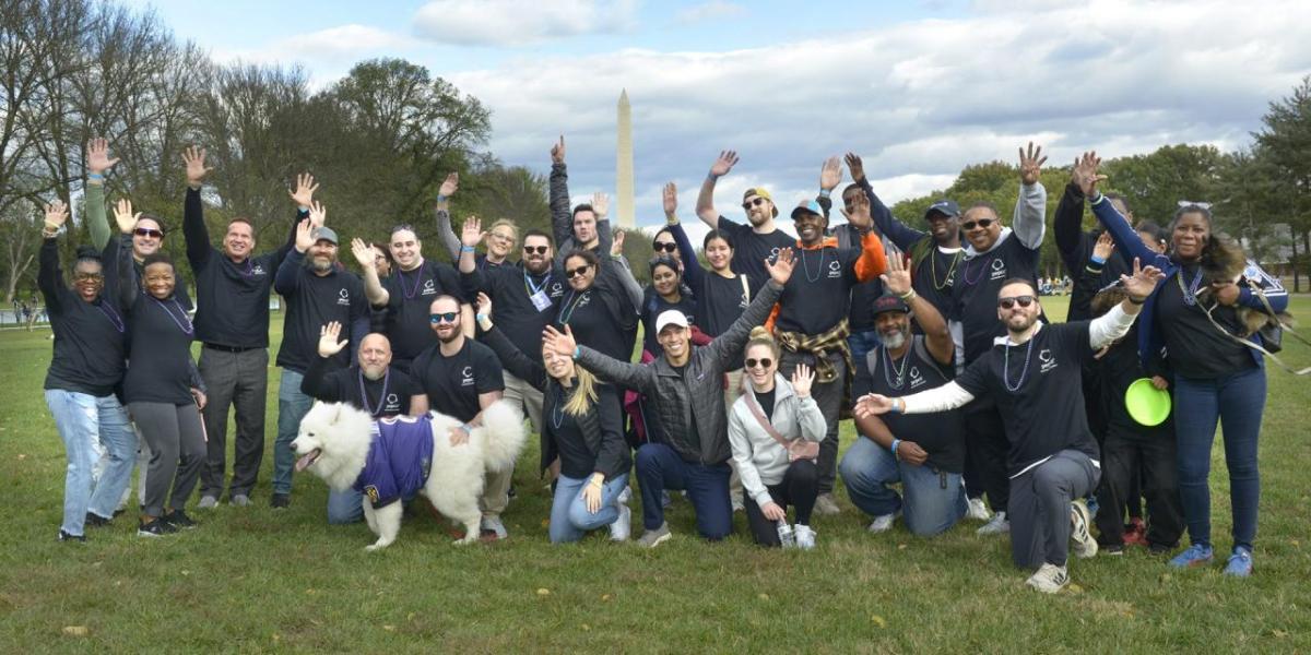 A group of people posed outside, smiling with raised hands. The Washington Monument in the distance.