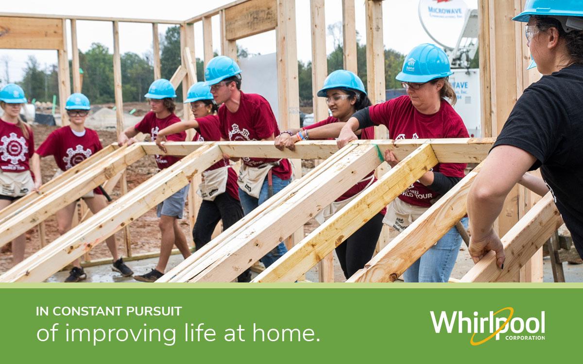 Volunteers lifting up framing for a house with text "In constant pursuit of improving life at home" with the Whirlpool logo