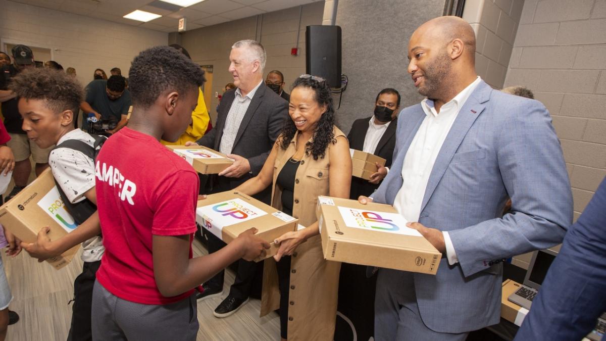 staff handing out Project UP laptops to kids