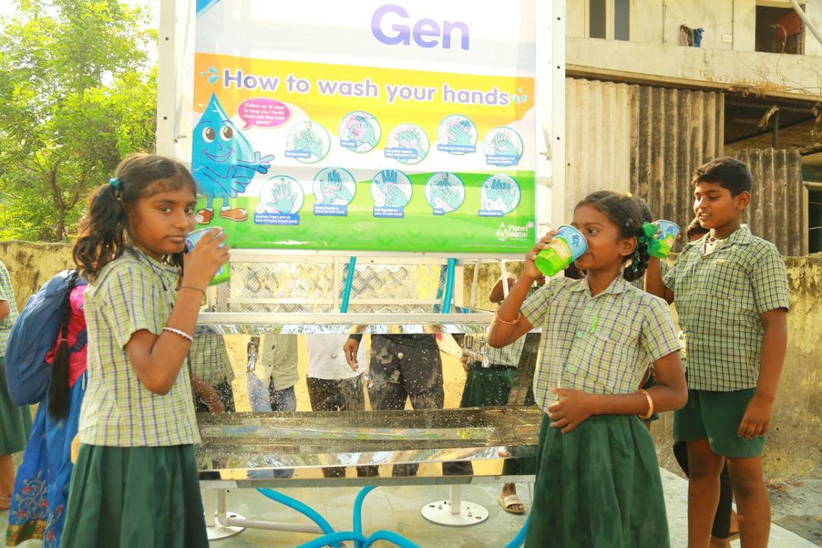 Three children drinking from cups at a water station.