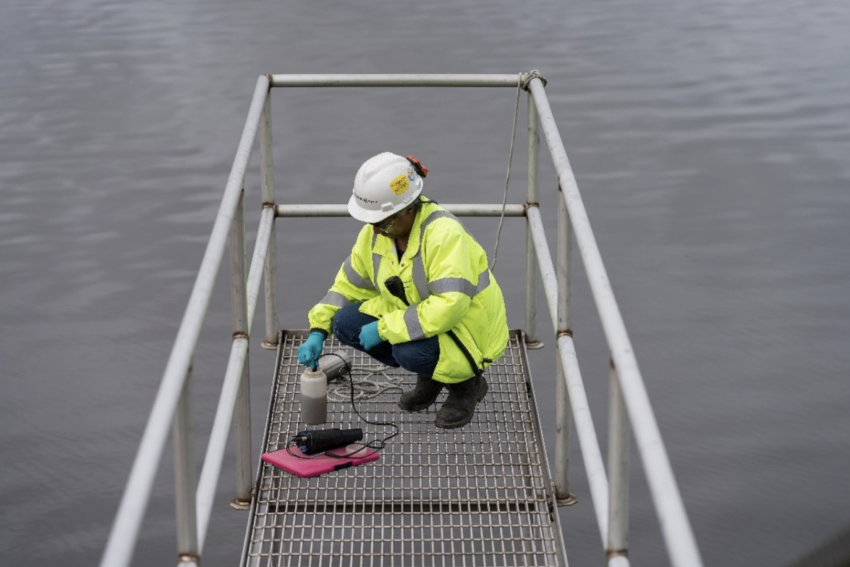 worker in safety gear crouched at the end of a metal catwalk over a body of water