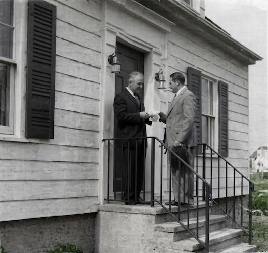 Webster Bank Founder Harold Webster Smith (pictured right with hat in hand) delivers the bank’s first loan to Joe Baltrush in December 1935 on the steps of his home at 114 Chambers Street in Waterbury.