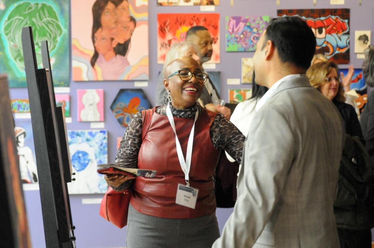 Two people standing in room with lots of artwork on the wall, and easels set up.