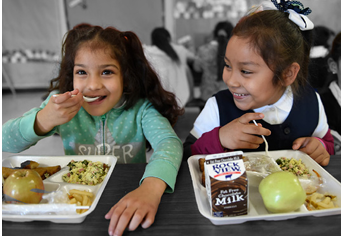 two smiling children eating a meal served on a tray