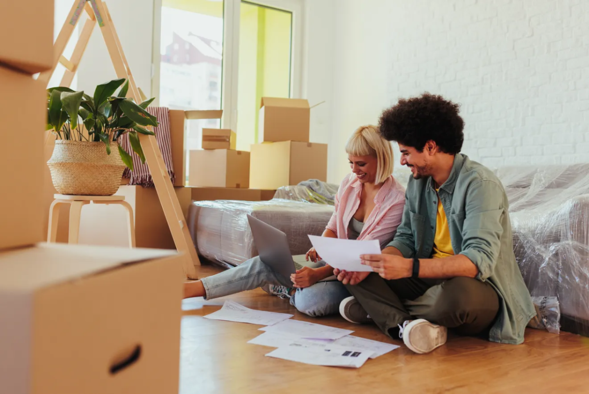 A couple sitting on the floor surrounded by moving boxes as they organize some paperwork