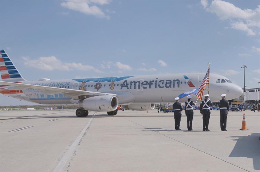 outside side view of American Air plane. Service members in uniform stand at attention on the tarmac