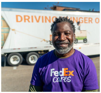 A smiling volunteer in front of a semi truck.