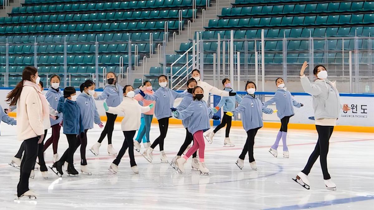 A group of children being led by an adult ice skating on a rink.