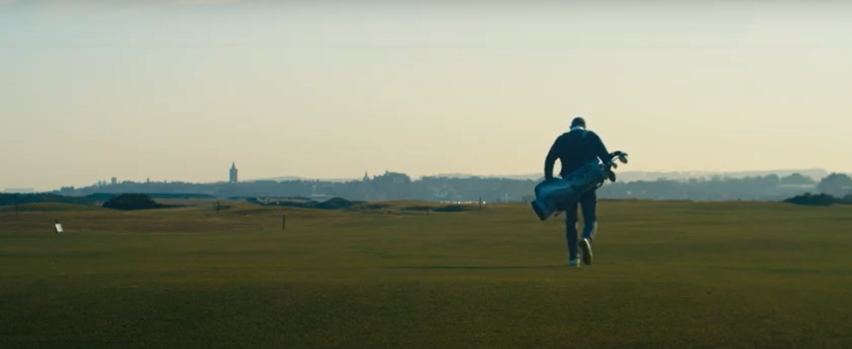 <a href=" https://bit.ly/3wHOLkU"target="_blank"> Click here to watch Carrying On, the Caddie School for Soldiers documentary </a> Rear view of caddy walking with golf clubs